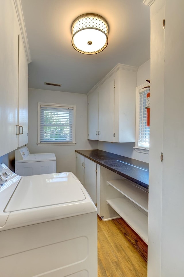 clothes washing area featuring light wood-style floors, cabinet space, separate washer and dryer, and visible vents