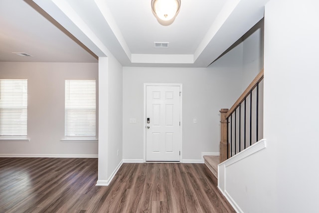 entrance foyer with a tray ceiling, visible vents, stairway, wood finished floors, and baseboards