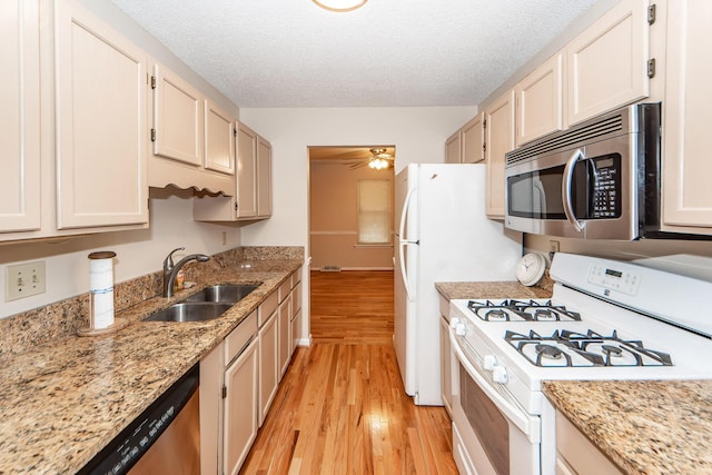 kitchen with light wood-type flooring, light stone countertops, appliances with stainless steel finishes, and sink