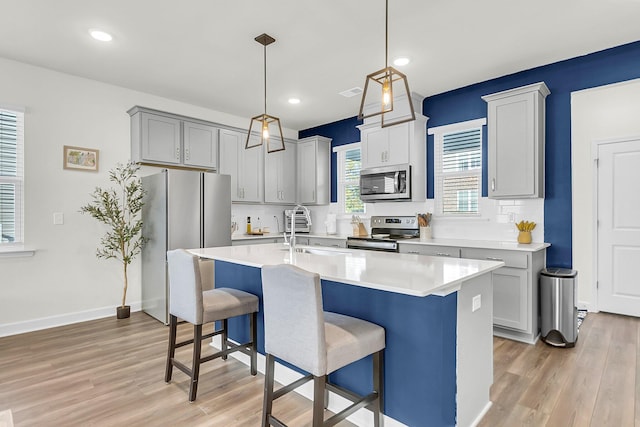 kitchen with gray cabinetry, sink, stainless steel appliances, an island with sink, and light wood-type flooring