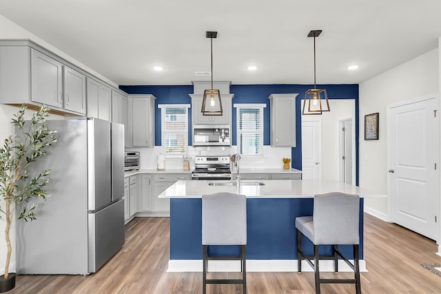 kitchen with a center island with sink, hardwood / wood-style flooring, gray cabinets, appliances with stainless steel finishes, and decorative light fixtures