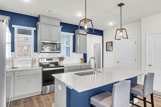 kitchen featuring sink, stainless steel appliances, plenty of natural light, decorative light fixtures, and a center island with sink