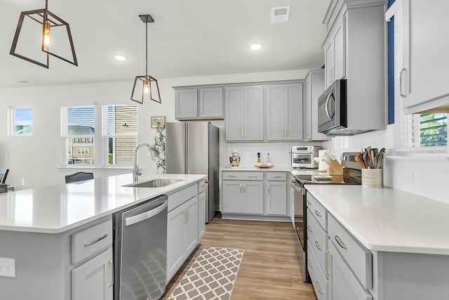 kitchen featuring appliances with stainless steel finishes, light hardwood / wood-style floors, pendant lighting, and sink