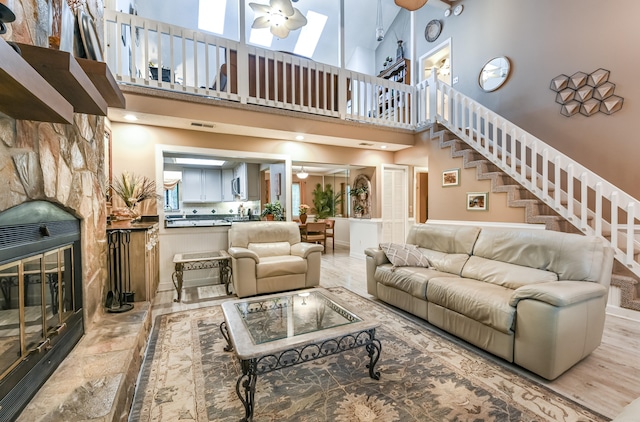 living room featuring a high ceiling, ceiling fan, and a stone fireplace