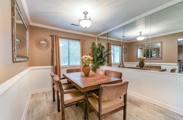 dining area with light wood-type flooring, a textured ceiling, and ornamental molding