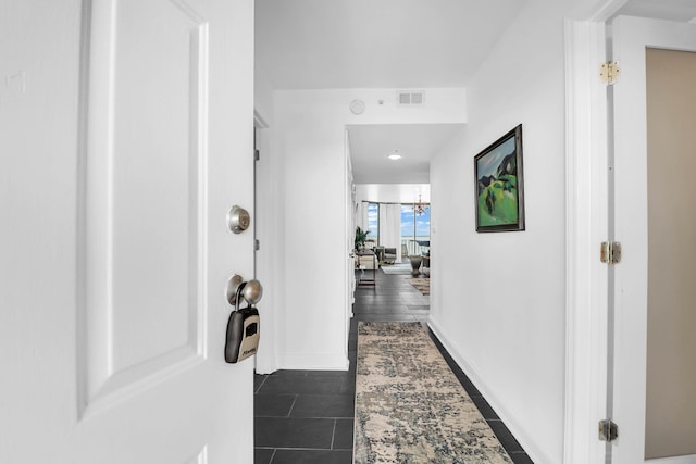 corridor featuring a chandelier and dark tile patterned flooring