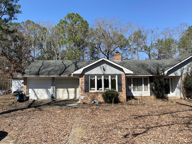 view of front facade with brick siding, driveway, a chimney, and an attached garage