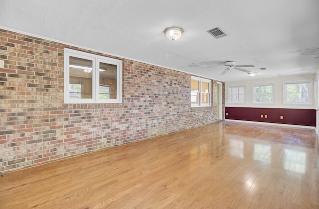 spare room with visible vents, brick wall, ceiling fan, a textured ceiling, and wood finished floors