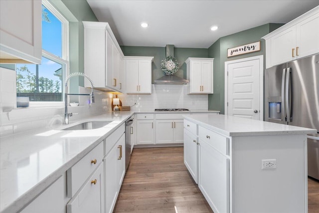 kitchen with white cabinets, wall chimney range hood, appliances with stainless steel finishes, tasteful backsplash, and a kitchen island