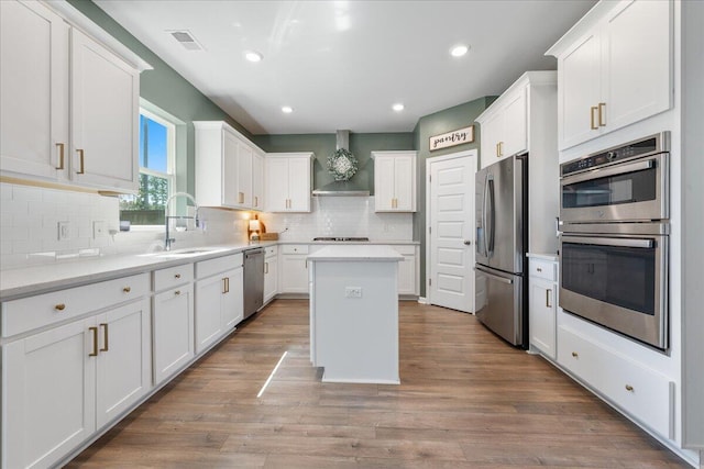 kitchen featuring wall chimney exhaust hood, a kitchen island, white cabinetry, and appliances with stainless steel finishes