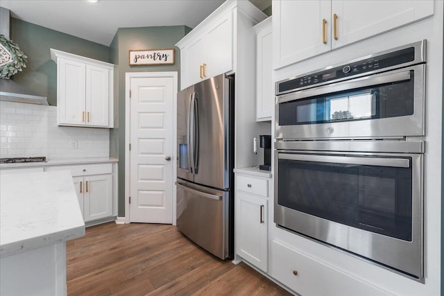 kitchen with backsplash, white cabinetry, stainless steel appliances, and light stone counters