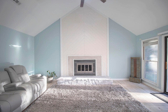 living room featuring high vaulted ceiling, beamed ceiling, a large fireplace, and light hardwood / wood-style flooring