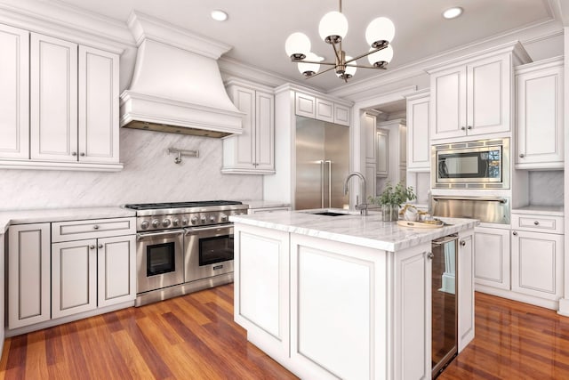 kitchen with sink, built in appliances, decorative light fixtures, custom range hood, and white cabinets