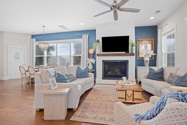 living room featuring ceiling fan with notable chandelier, a large fireplace, a healthy amount of sunlight, and hardwood / wood-style floors