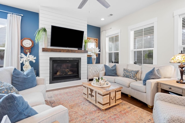 living room featuring ceiling fan, a large fireplace, a healthy amount of sunlight, and hardwood / wood-style floors