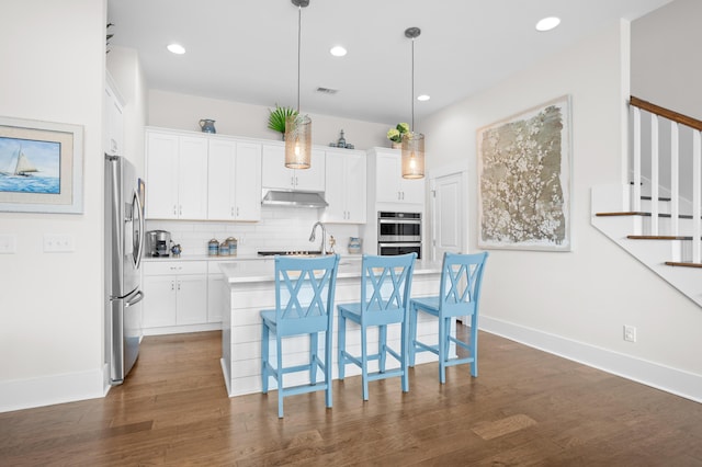 kitchen with stainless steel appliances, a kitchen island with sink, pendant lighting, and white cabinets