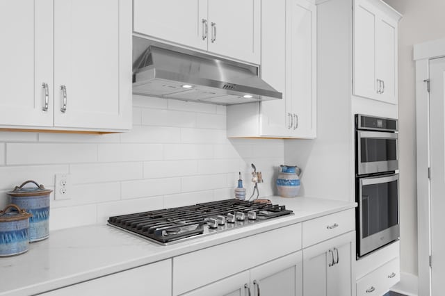 kitchen featuring white cabinets, backsplash, exhaust hood, light stone counters, and stainless steel appliances