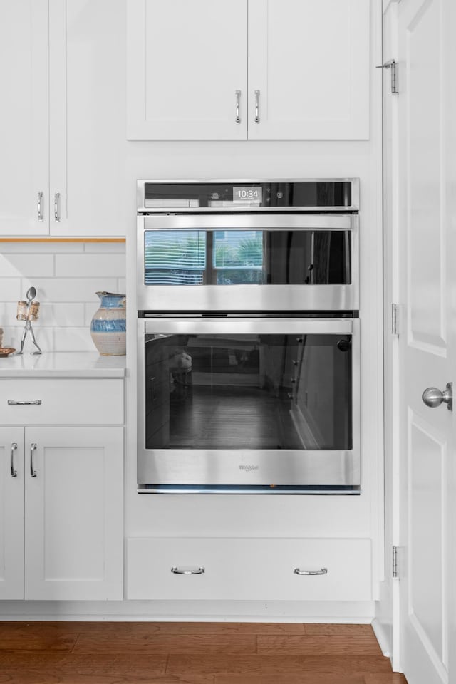 kitchen featuring white cabinetry, light stone counters, tasteful backsplash, double oven, and hardwood / wood-style flooring