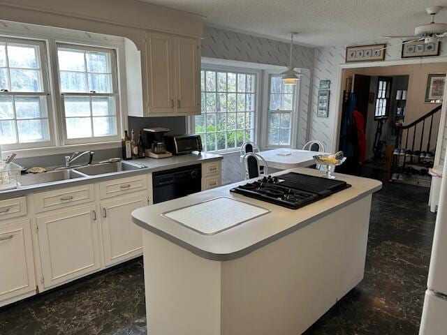 kitchen featuring light countertops, a kitchen island, white cabinets, black appliances, and a sink