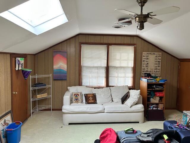 living area featuring wood walls, vaulted ceiling with skylight, ceiling fan, and carpet