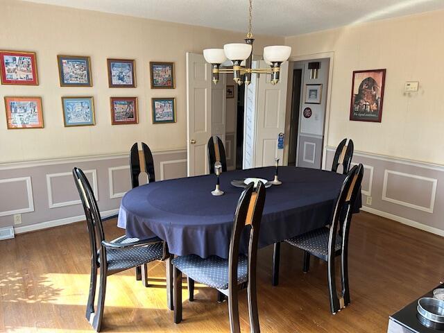 dining space featuring a chandelier, a decorative wall, wood finished floors, and wainscoting