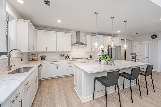 kitchen featuring white cabinetry, sink, a center island, stainless steel appliances, and wall chimney range hood