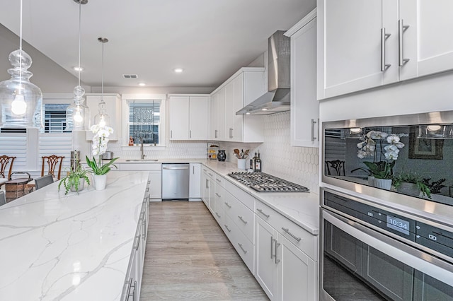 kitchen with white cabinetry, appliances with stainless steel finishes, wall chimney exhaust hood, and pendant lighting