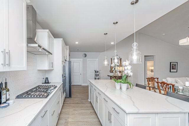 kitchen featuring stainless steel gas stovetop, decorative light fixtures, a kitchen island, and wall chimney range hood