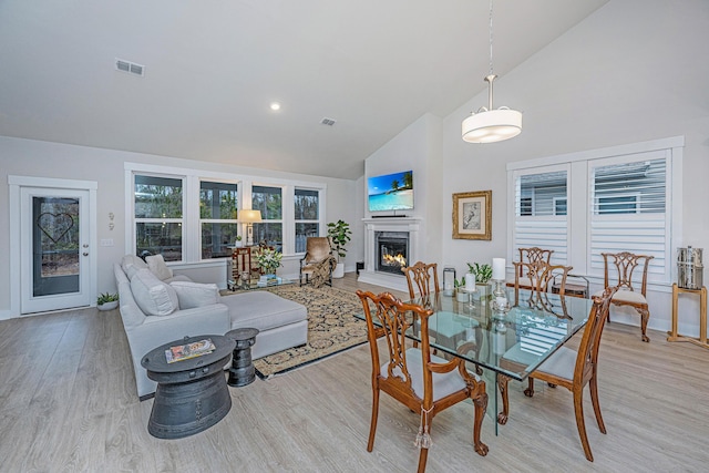 dining area featuring a high end fireplace, high vaulted ceiling, and light hardwood / wood-style flooring