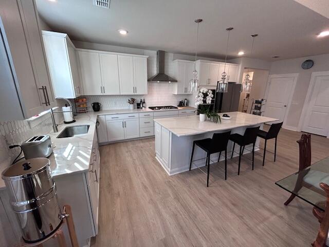 kitchen with a kitchen island, white cabinetry, sink, hanging light fixtures, and wall chimney range hood