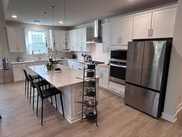 kitchen with white cabinetry, appliances with stainless steel finishes, a center island, and wall chimney exhaust hood