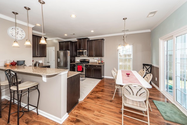 kitchen featuring light stone counters, stainless steel appliances, a peninsula, hanging light fixtures, and a kitchen bar