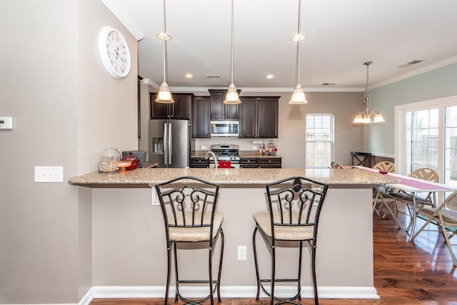 kitchen with hanging light fixtures, dark brown cabinetry, appliances with stainless steel finishes, and a breakfast bar area