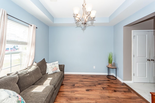 living room featuring an inviting chandelier, a raised ceiling, and baseboards