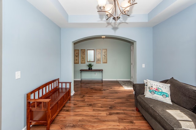 living room featuring a raised ceiling, a notable chandelier, baseboards, and wood finished floors