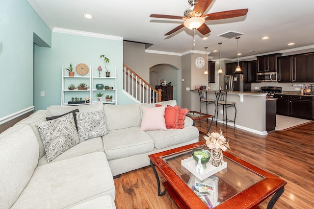 living room with arched walkways, visible vents, stairway, light wood-type flooring, and crown molding