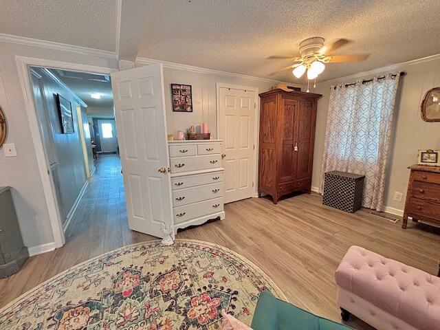 bedroom featuring a textured ceiling, ornamental molding, light wood-style floors, baseboards, and a ceiling fan