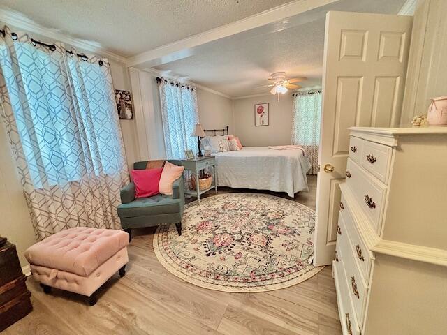 bedroom featuring ornamental molding, light wood-style floors, a textured ceiling, and a ceiling fan