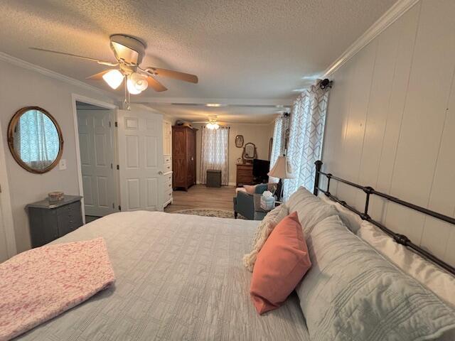bedroom with a textured ceiling, multiple windows, ceiling fan, ornamental molding, and wood finished floors