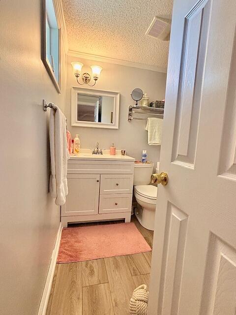 half bathroom featuring a textured ceiling, wood finished floors, toilet, vanity, and crown molding