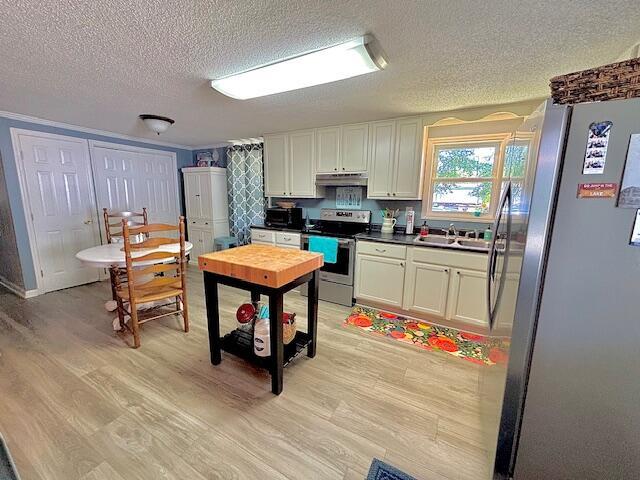 kitchen featuring appliances with stainless steel finishes, a textured ceiling, under cabinet range hood, light wood-style flooring, and a sink