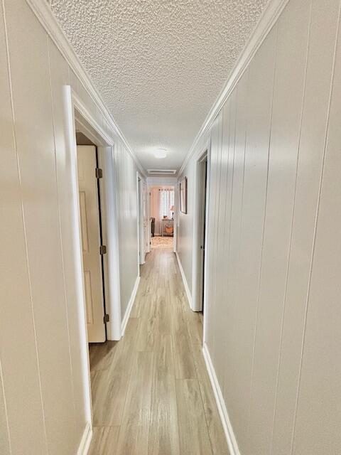 corridor featuring light wood-style floors, ornamental molding, a textured ceiling, a decorative wall, and baseboards