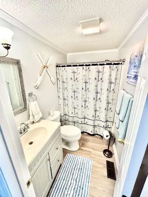 full bathroom with a textured ceiling, vanity, wood finished floors, crown molding, and toilet