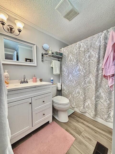bathroom featuring a textured ceiling, wood finished floors, vanity, toilet, and a shower with shower curtain