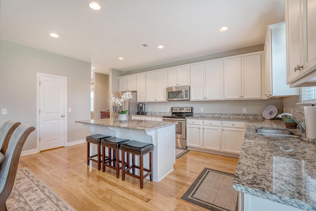 109 Cypress Plantation Rd, Moncks Corner, SC 29461 - kitchen with stainless steel appliances, a kitchen bar, white cabinetry, light wood finished floors, and recessed lighting