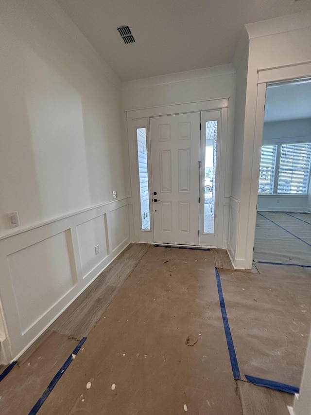 foyer entrance with wainscoting, visible vents, and crown molding