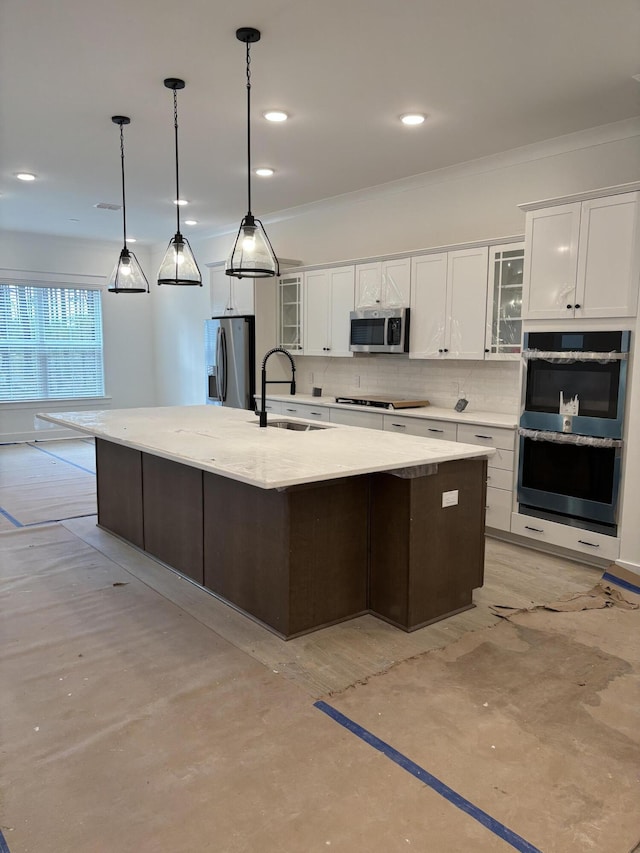 kitchen with decorative backsplash, appliances with stainless steel finishes, a large island with sink, white cabinetry, and a sink