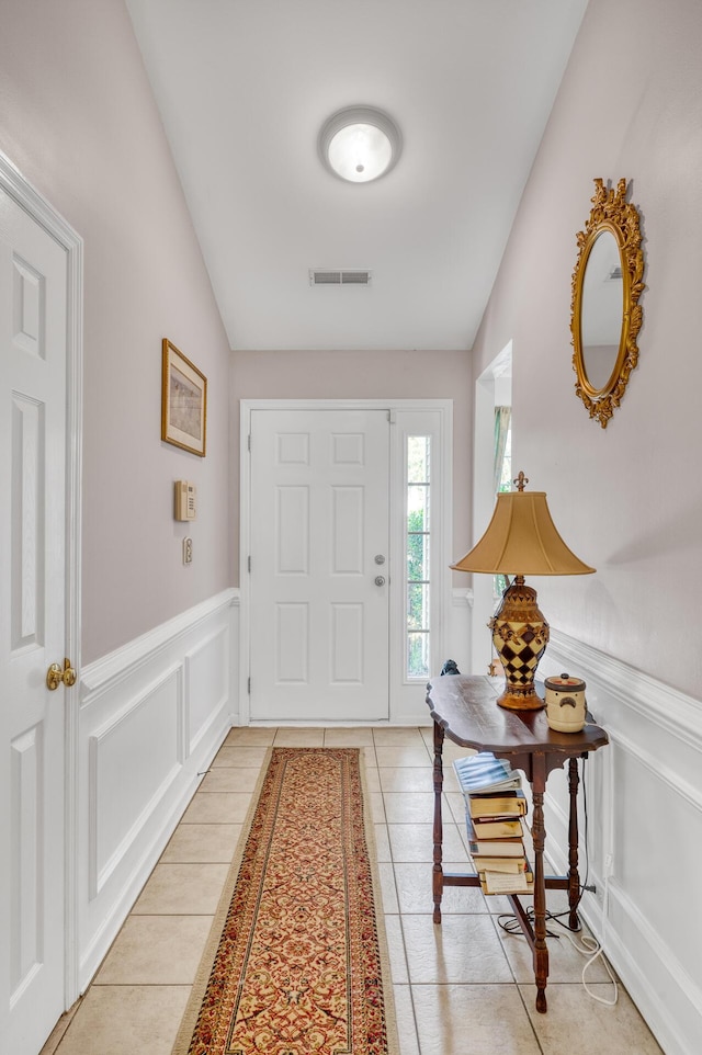 foyer entrance featuring light tile patterned floors, visible vents, vaulted ceiling, and wainscoting