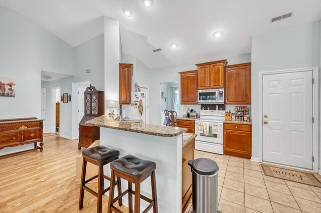 kitchen with light hardwood / wood-style flooring, white appliances, light stone counters, kitchen peninsula, and a kitchen breakfast bar