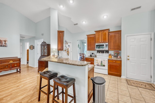 kitchen with visible vents, stainless steel microwave, electric range, a peninsula, and a kitchen bar